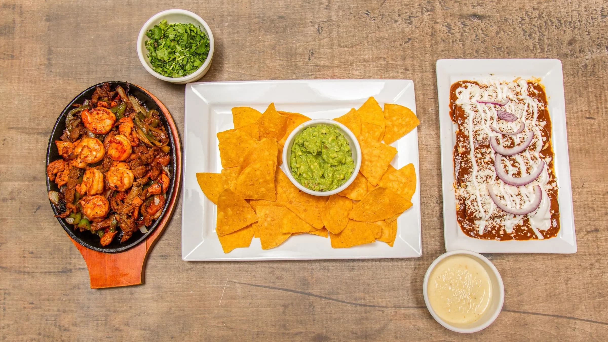 Shrimp and steak fajitas on a sizzling skillet with chips, guacamole and enchiladas in mole sauce